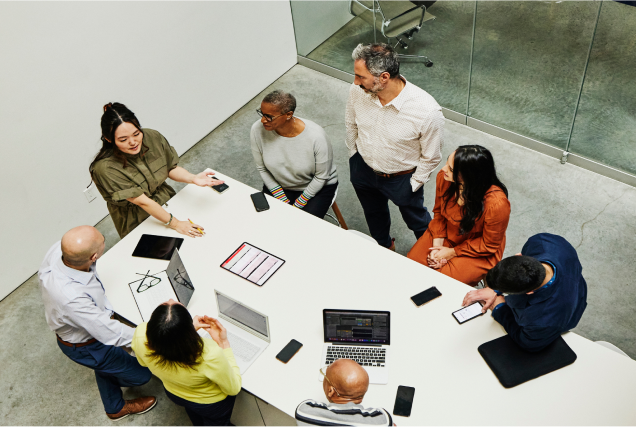 employees gathered around conference room table with laptops and tablets